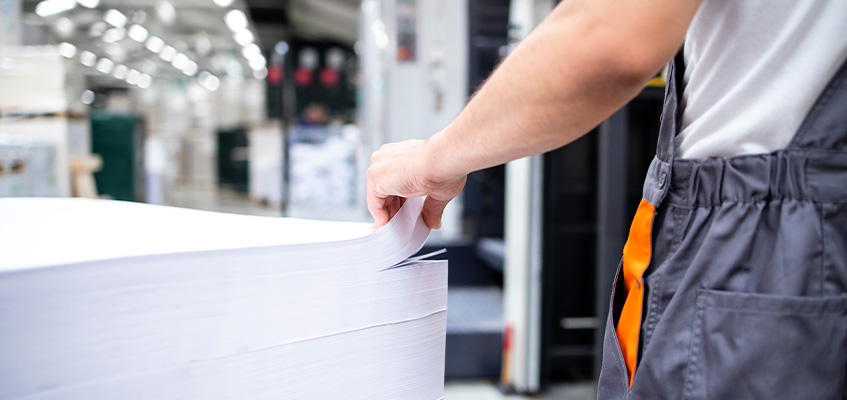 A print worker standing besides a stack of paper